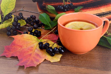Autumn composition. An orange cup with tea and lemon on a wooden table. Chokeberry and multicolored maple leavesの写真素材