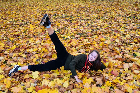 beautiful girl in jumper and scarf is lying on the ground among autumn leaves and doing exercises, physical education, doing sports, enjoying nature. Recreation and outdoor activitiesの写真素材