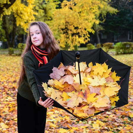 beautiful girl in a sweater and scarf holds an umbrella filled with yellow autumn leaves. Teenage girl walks in an autumn park and enjoys natureの写真素材