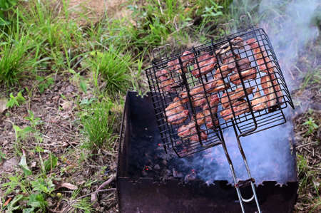 Photo of cooking fry shish kebab, barbecue, meat on coals. Delicious crispy meat barbecue on metal grill. Trip to nature in summer for picnic. Copy spaceの写真素材