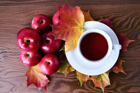 Autumn composition of red apples and yellow maple leaves lying on wooden table and white cup of tea. Flat layout with a top view. Hello, September!の写真素材