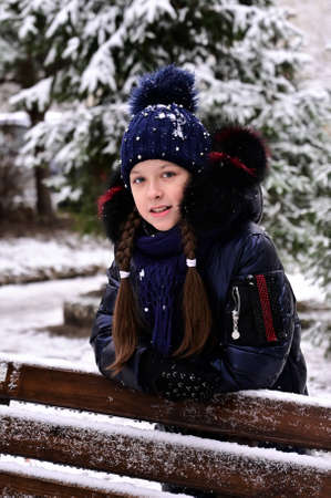 girl in winter clothes at a bench in a winter parkの写真素材