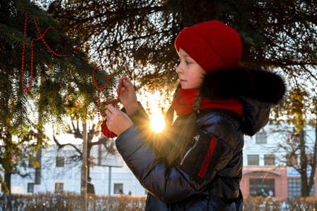 a girl at a natural Christmas tree with a Christmas toy in her hands in winter