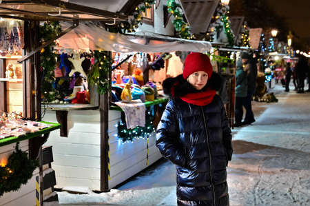 pretty young girl in red hat and scarf stands against background of winter New Year's fair. Buying gifts for Christmas. New Year's salesの写真素材