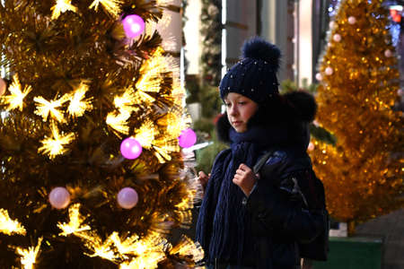a girl looks at a beautiful artificial Christmas tree in the evening cityの写真素材