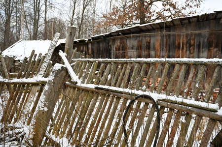 rickety old fence in abandoned village. Cold late autumn and first snow in countrysideの写真素材