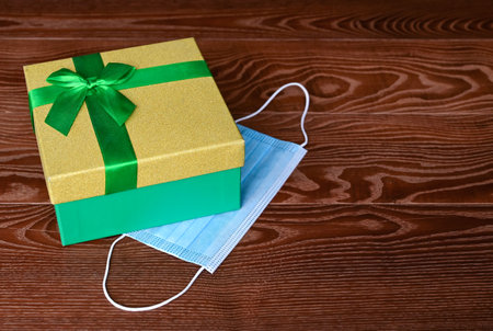 medical mask and a gift box with green ribbon on wooden background. Choosing and buying gifts in...