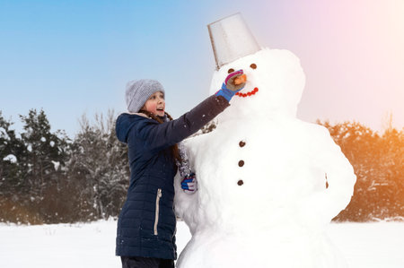 Cute girl makes snowman on winter day. Girl on a snow-covered field in the open air. Artistically colored and tinted photographyの写真素材