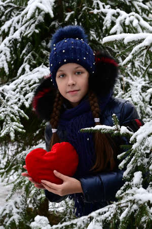 a girl holds a red heart in her hands in a winter park. Valentine's dayの写真素材