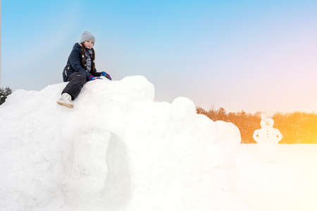 teenage girl playing with snow on a winter day, sitting on a snow fortress, a snowman in the...
