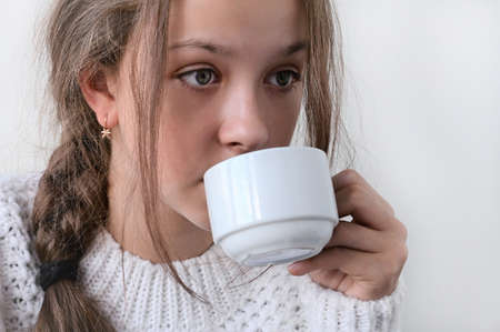 pretty girl in knitted warm sweater drinks from white cup, warms up. Concept of winter rest and...