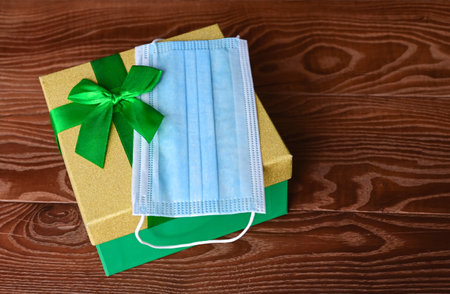 medical mask and a gift box with green ribbon on wooden background. Choosing and buying gifts in quarantine. Holiday sale. Copy spaceの写真素材