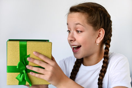 happy teenage girl with long braids holds gift in beautiful box, looks at it and rejoices. Happy birthday, Merry Christmas. Selective focusの写真素材