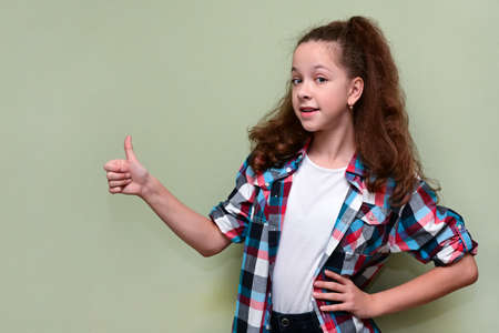 portrait of pretty teenage girl in white T-shirt and plaid shirt shows raised thumb, expressing her consent. Copy spaceの写真素材