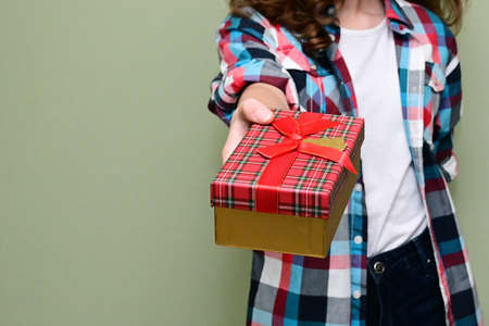 hand of teenage girl in plaid shirt holds out a gift box with surprise. Concept of celebrating birthday or Christmas. Copy spaceの写真素材
