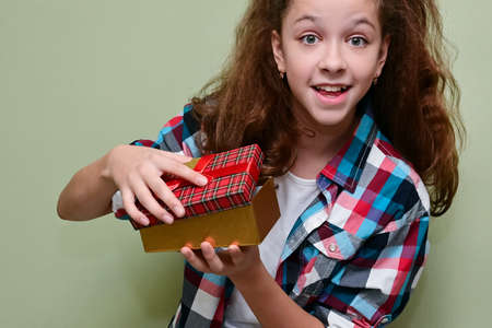 joyful, happy teenage girl in plaid shirt holds surprise gift box in her hands and opens it. Congratulations on holiday. Copy spaceの写真素材