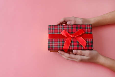 girl's hands are holding gift box tied with red ribbon with bow on pink background. Gifts for holiday. Valentine's day. Copy spaceの写真素材