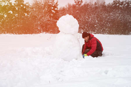 A man makes a snowman in a snow-covered field in the open air. Winter time. Artistically colored and tinted photographyの写真素材