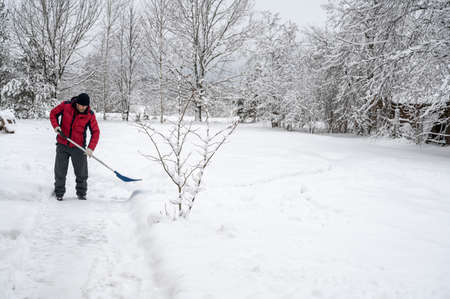 man in a red jacket clears the road from snow with a shovel in the village. Winter worries