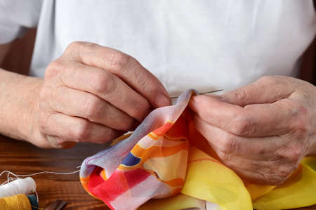 hands of an elderly woman hold a sewing needle. Tailor's hands at work close-up. Handmade work. Needlework and sewingの写真素材