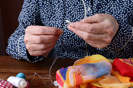 hands of an elderly woman with sewing needle and button. Tailor's hands at work close-up. Handmade work. Needlework and sewingの写真素材