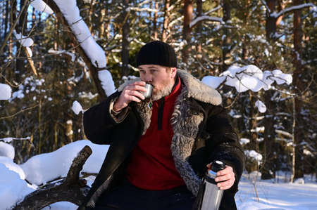 Portrait of brutal man with beard. Adult man is holding thermos with cup of hot tea, drinking...