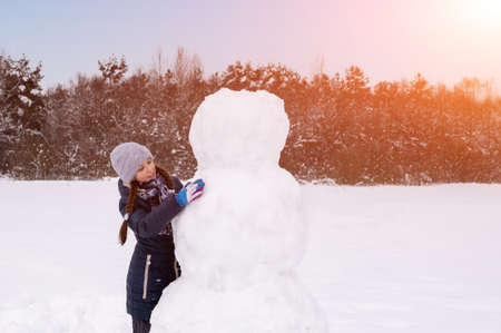 Cute girl makes snowman on winter day. Girl on a snow-covered field in the open air. Artistically colored and tinted photographyの写真素材