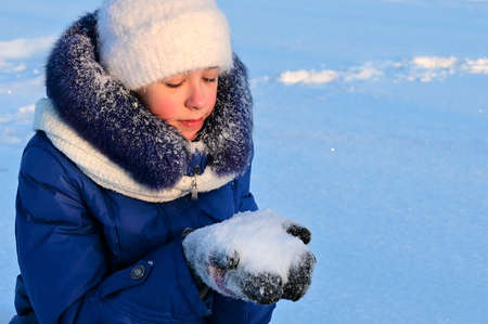 Portrait of pretty girl in warm clothes in rays of winter sun. Girl holds snow in her palms and...