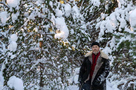 brutal man with beard in warm unbuttoned sheepskin coat makes his way through large snowdrifts of winter snow-covered forest. life in country sideの写真素材