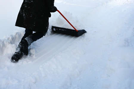 man cleans snow with large shovel-scraper in suburbs. Clearing the road in winter after a snowstorm. Winter timeの写真素材