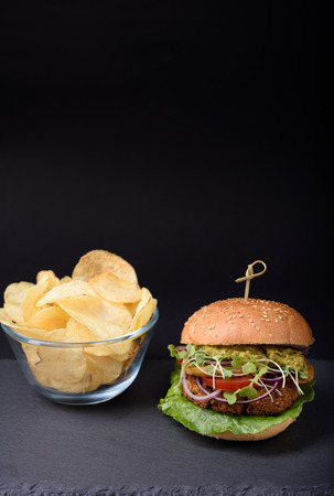 Homemade burger with crispy potato chips on slate board over black background. Free text space.の写真素材