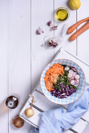 Carrot salad with cabbage and radish in blue ceramic bowl over white wooden table, top view. Dieting, clean eating, vegan, vegetarian food conceptの写真素材