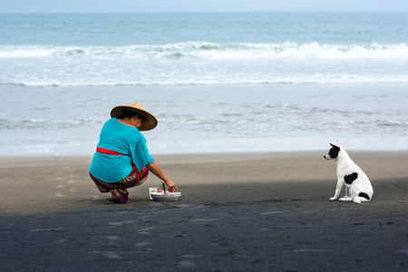 Balinese woman on a black volcanic sand of Echo Beach making daily nature-based worship of Balinese Hinduism. Echo Beach, Canggu, Bali, Indonesia 02 October 2016.のeditorial素材