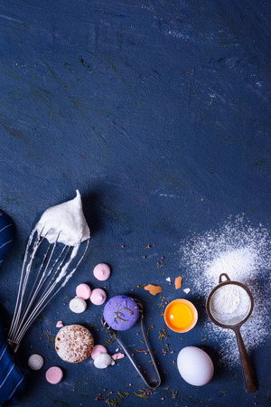 Bakery ingredients - flour, eggs, sugar, yolk, macaroni dessert on blue table. Sweet pastry party baking concept. Flat lay, copy space, top view.の写真素材