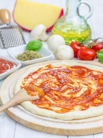Pizza dough with tomato sauce on a wooden boardの写真素材