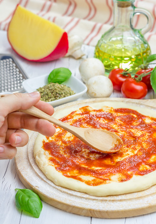 Pizza dough with tomato sauce on a wooden boardの写真素材
