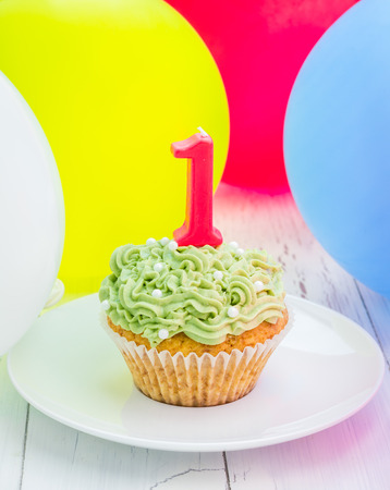 Homemade tasty birthday cupcake with candle, colorful balloons on backgroundの写真素材