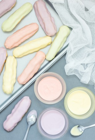 Homemade eclairs with pastel color icing on a baking sheetの写真素材