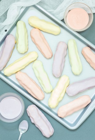 Homemade eclairs with pastel color icing on a baking sheet