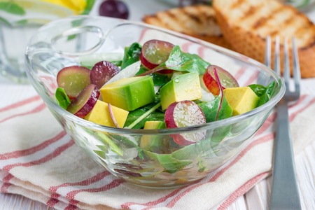 Vegetarian salad with avocado, grape, rucola, onion with vinegar dressing, in glass bowl, horizontalの写真素材