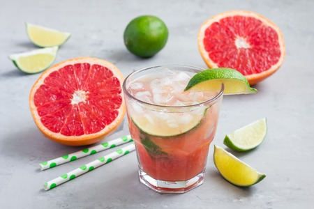 Cold pink cocktail with fresh grapefruit, lime and ice cubes on concrete background, paloma