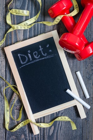 Black chalkboard for copy space with pieces of chalk, tape measure and dumbbells, healthy eating and dieting concept, verticalの写真素材
