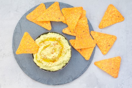 Healthy avocado hummus sprinkled with olive oil, paprika and sesame, served with nachos, horizontal, top viewの写真素材