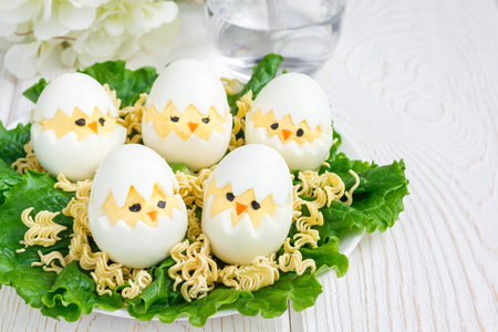 Little chicken in nest, deviled eggs served with salad and dry ramen on white plate, horizontal, copy spaceの写真素材