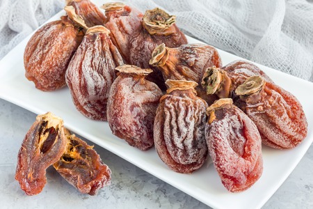 Several dried persimmon on white plate, gray concrete background, horizontalの写真素材