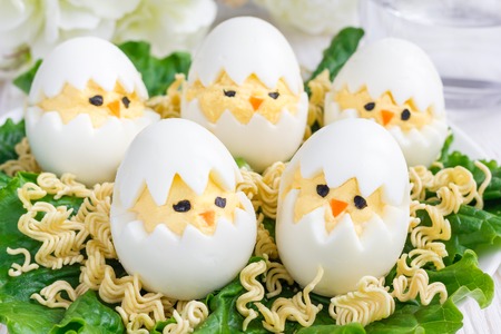 Little chicken in nest, deviled eggs served with salad and dry ramen on white plate, horizontalの写真素材
