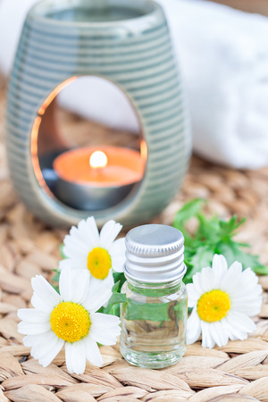 Chamomile essential oil in glass on woven mat with spa background, verticalの写真素材