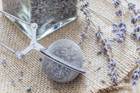 Dry lavender tea in tea infuser spoon and glass jag on wooden background, horizontal, closeupの写真素材