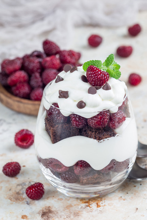 Trifle dessert with brownie, cream cheese frosting and raspberry in a glass, verticalの写真素材