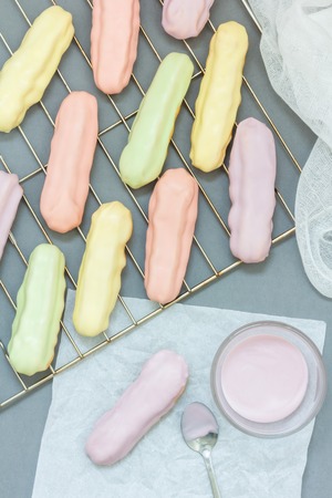 Homemade eclairs with pastel color icing on a cooling rack, verticalの写真素材